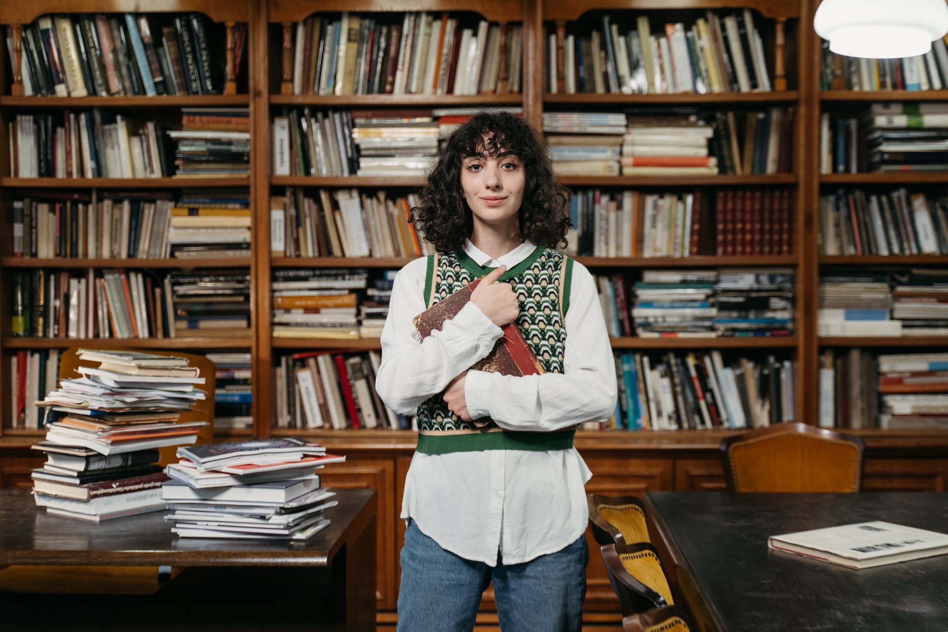 a woman wearing a vest over a dress shirt holding a book